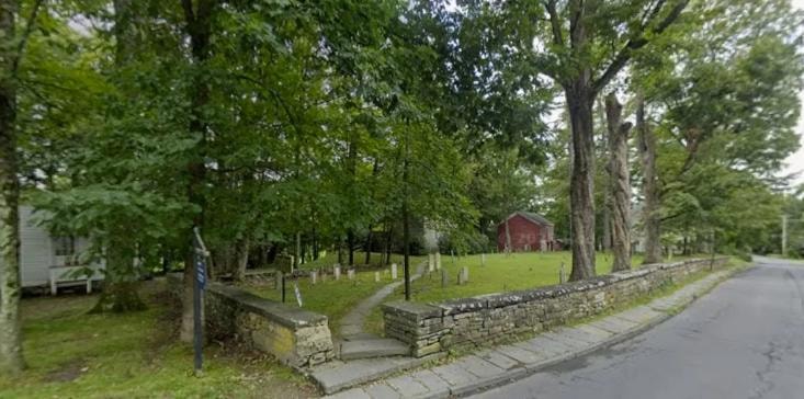 Huguenot Cemetery (Old Huguenot Burying Ground) at 60 Huguenot St, New Paltz — stone wall entrance, gravestones, and red barn visible through mature trees